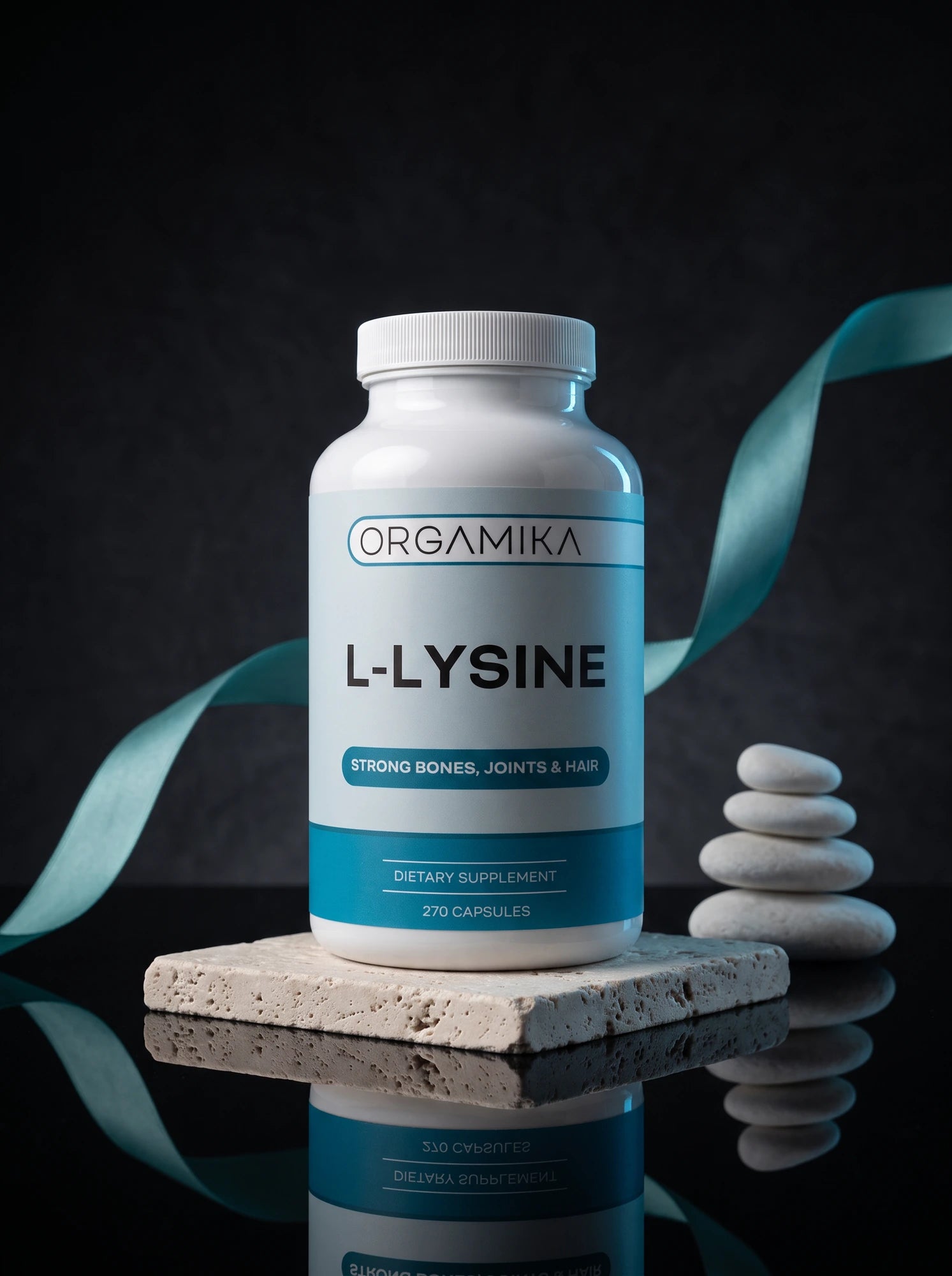 The white ORGAMIKA L-Lysine 270 capsule bottle lit against a near-black studio backdrop, standing on a travertine slab beside stacked river stones and a teal ribbon