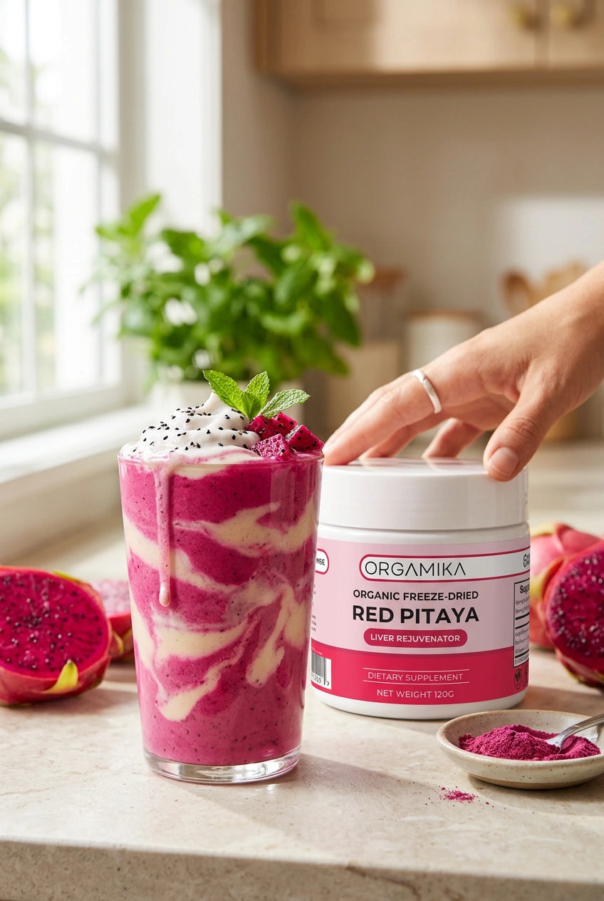A vivid pink dragon fruit smoothie beside the ORGAMIKA Red Pitaya tub, fresh dragon fruit halves and a dish of magenta powder on a kitchen counter