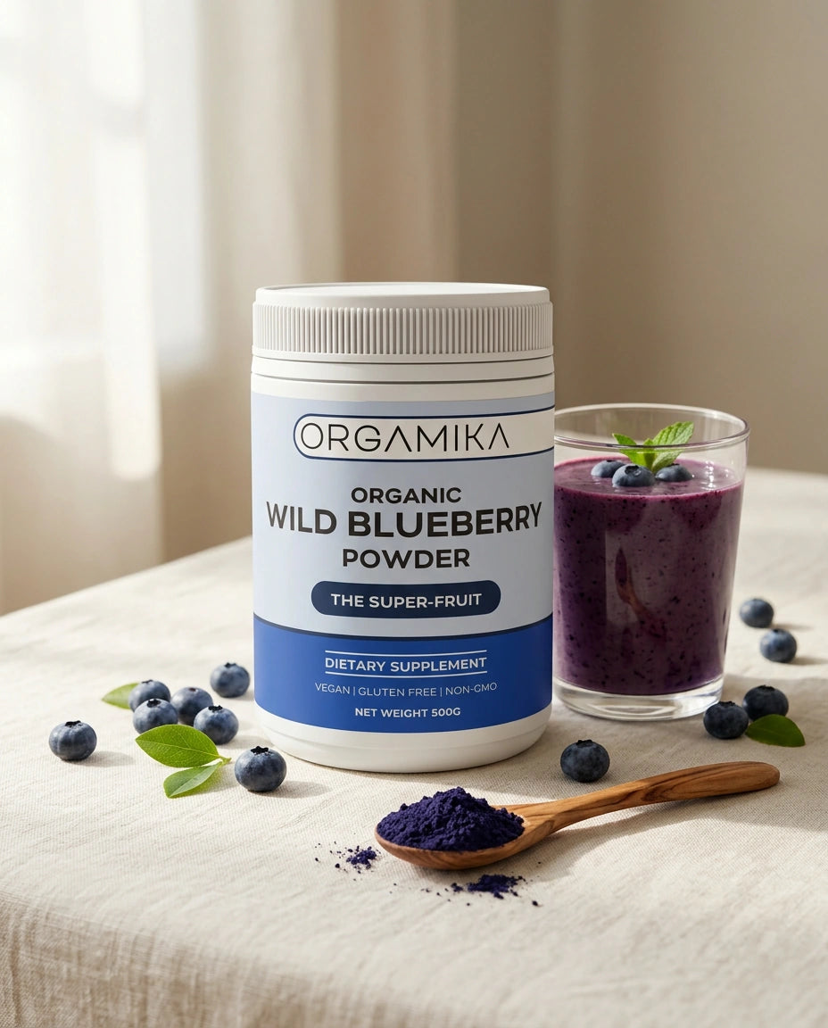 The ORGAMIKA Wild Blueberry Powder tub on a linen table with fresh blueberries, a wooden spoon of deep violet powder and a blueberry smoothie